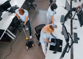 Top view. Group of workers clean modern office together at daytime.